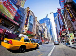 Fish eye still of a street in New York city filled with traffic and a clear view of buildings and advertisements. 