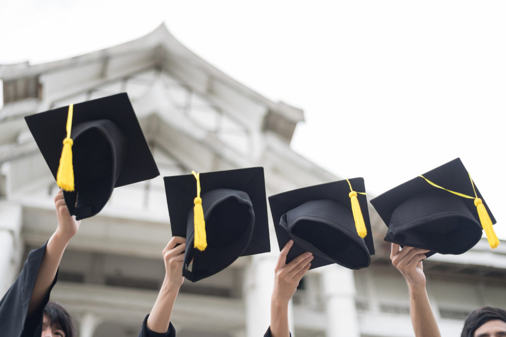 Group of college graduates lift their caps in the air as they prepare to receive their diplomas.