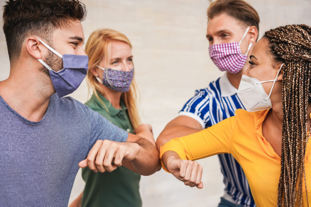 Young people friends bump their elbows instead of greeting with a hug - Avoid the spread of coronavirus, social distance and friendship concept - Wearing promotional item masks