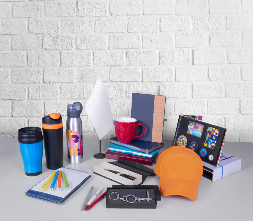 Various promotional products such as a hat, water bottles, and notebooks on a white table in El Paso.