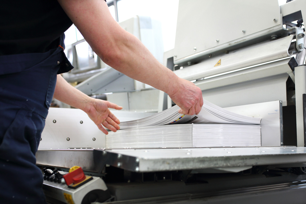 A person lifting up a stack of papers that have been printed at a print shop in El Paso.